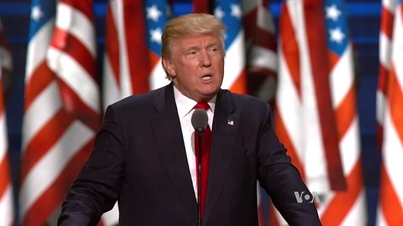 Donald Trump delivering a speech with American flags in the background